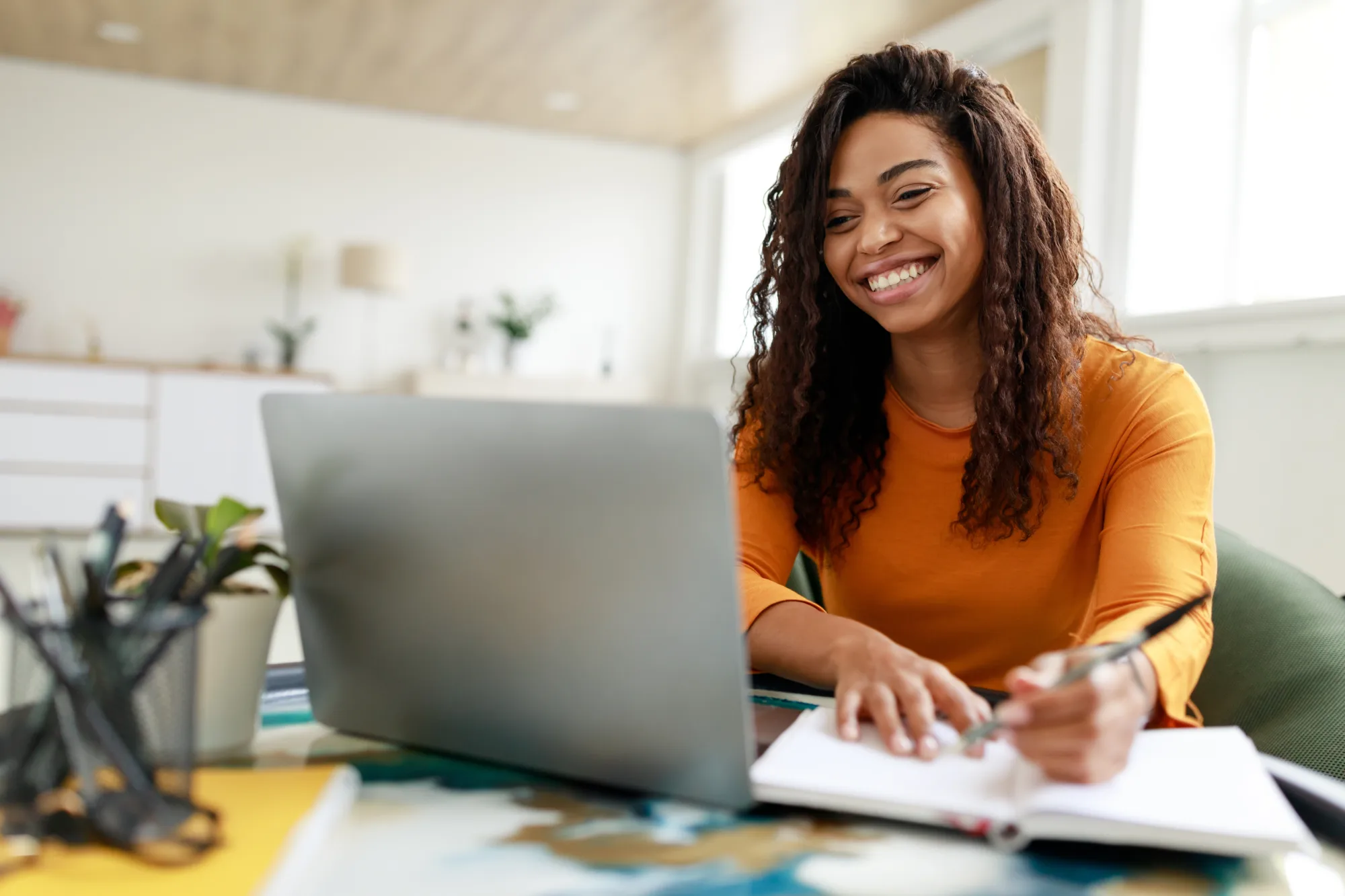 Smiling woman participating in Palmetto Goodwill Employment Services training online with a laptop and notebook.