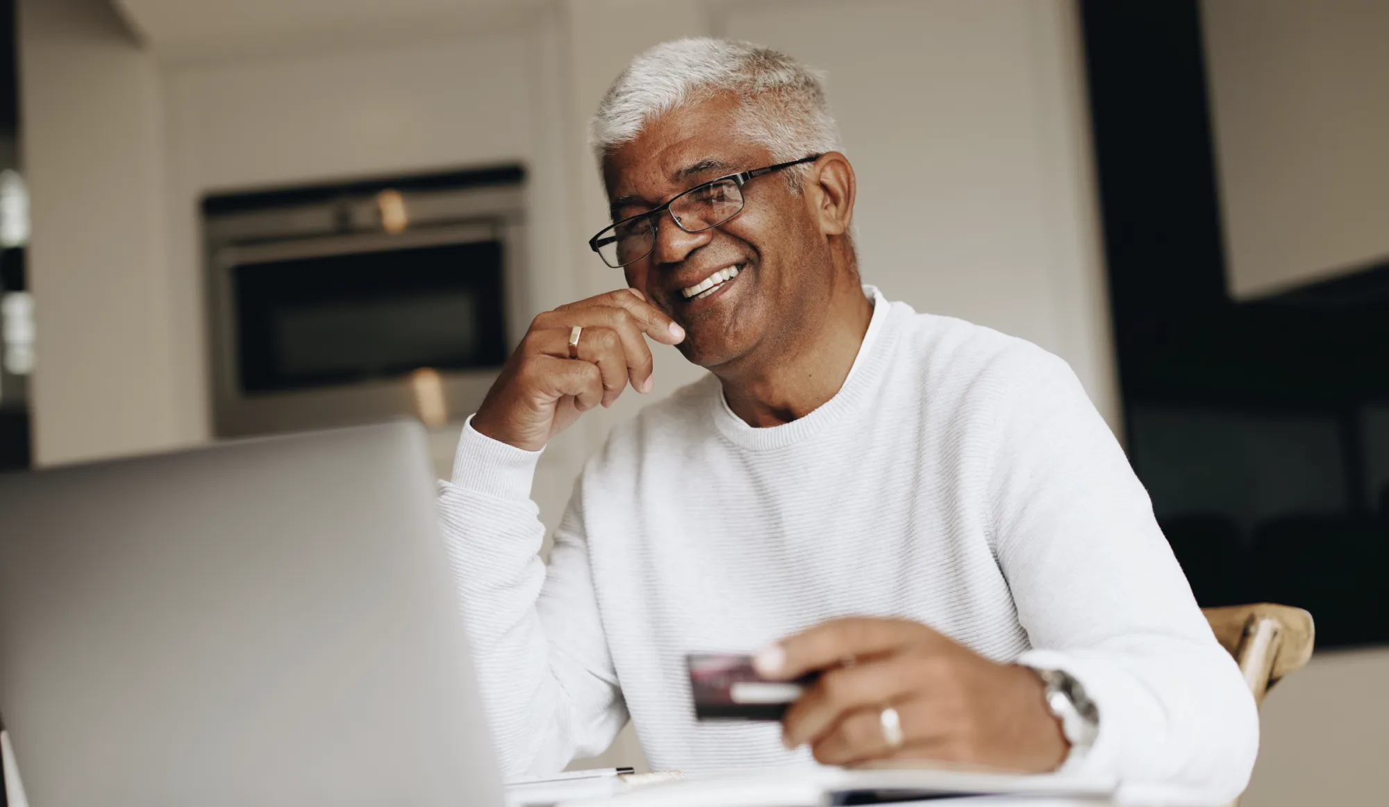 Smiling man making an online donation to Palmetto Goodwill, holding a credit card while using a laptop.