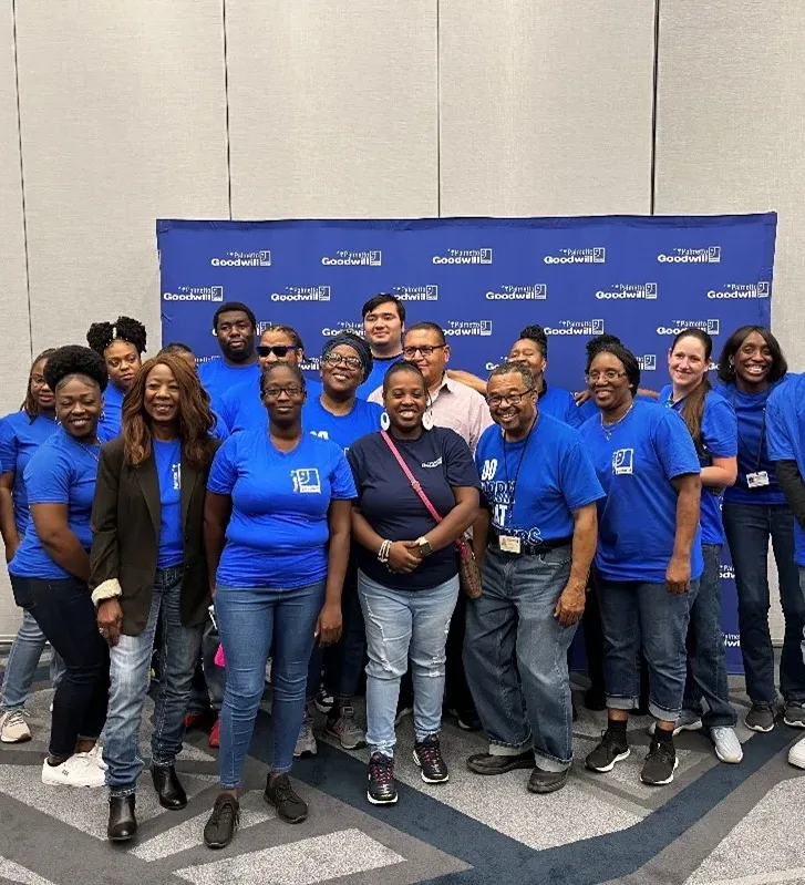 Goodwill employees and staff wearing blue shirts and jeans, standing together for a team photo at a conference or event.