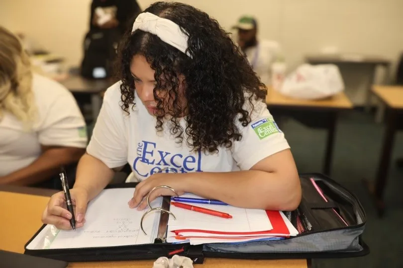 An adult student at The Palmetto Excel Center focusing on writing notes in a classroom setting.