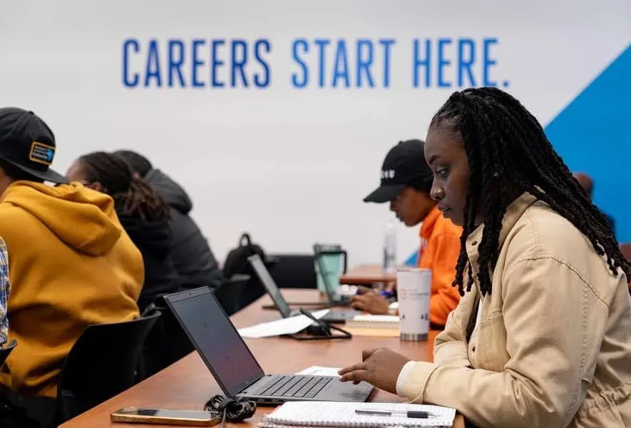 Students utilizing laptops for free Google and Coursera Career Training from Palmetto Goodwill in a class with a 'Careers Start Here' sign.