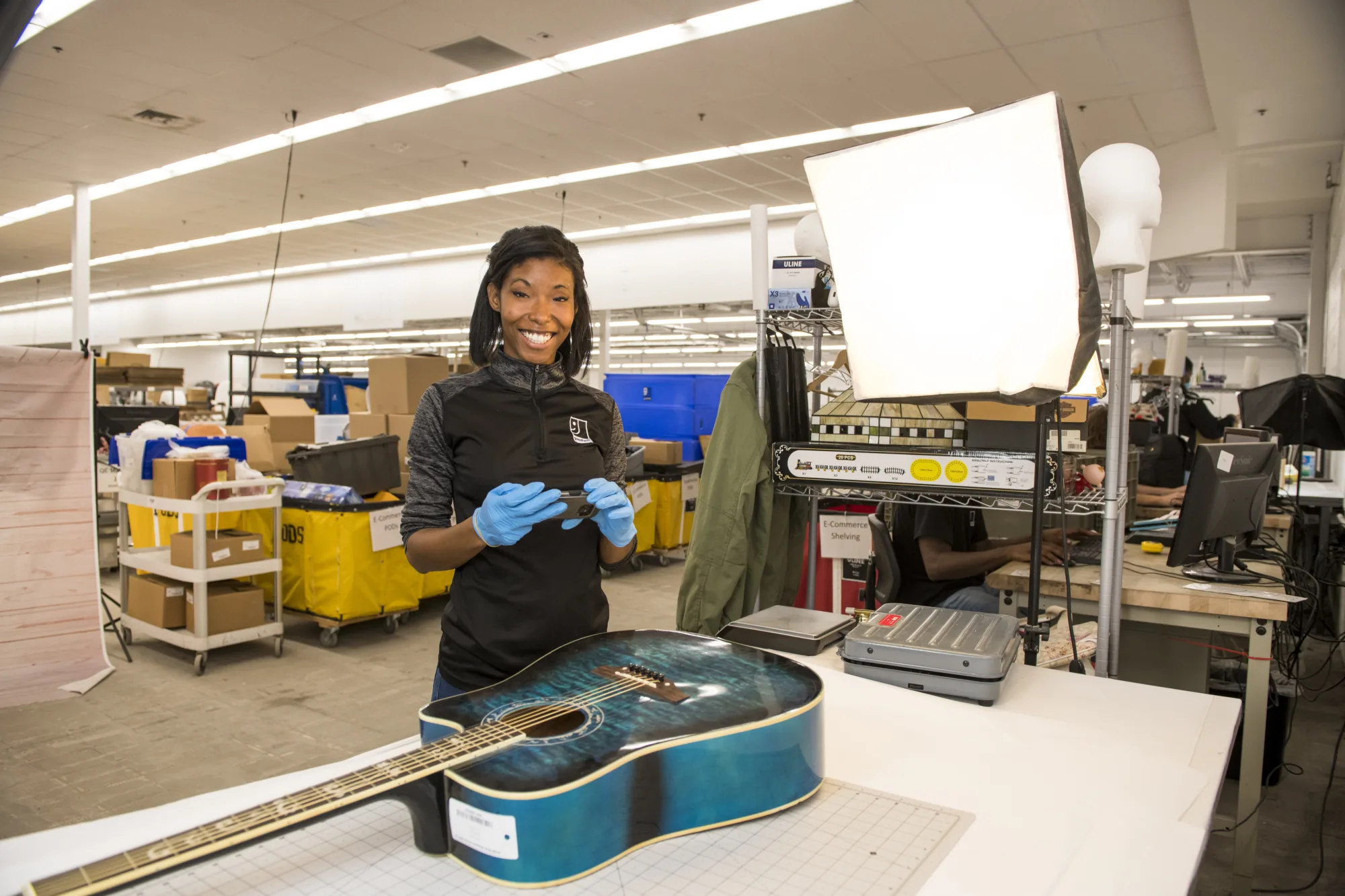 Palmetto Goodwill E-commerce team member photographing a blue acoustic guitar for sale on ShopGoodwill.com or the eBay store.