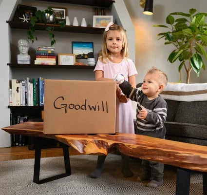 Two young children standing next to a large cardboard box labeled 'Goodwill' for donations.