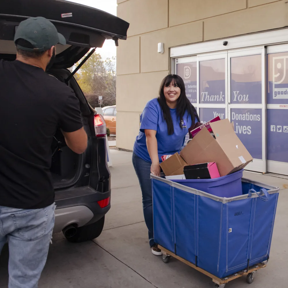 A Palmetto Goodwill employee is cheerfully collecting boxes of donations from a donor's car at the drive-up center.