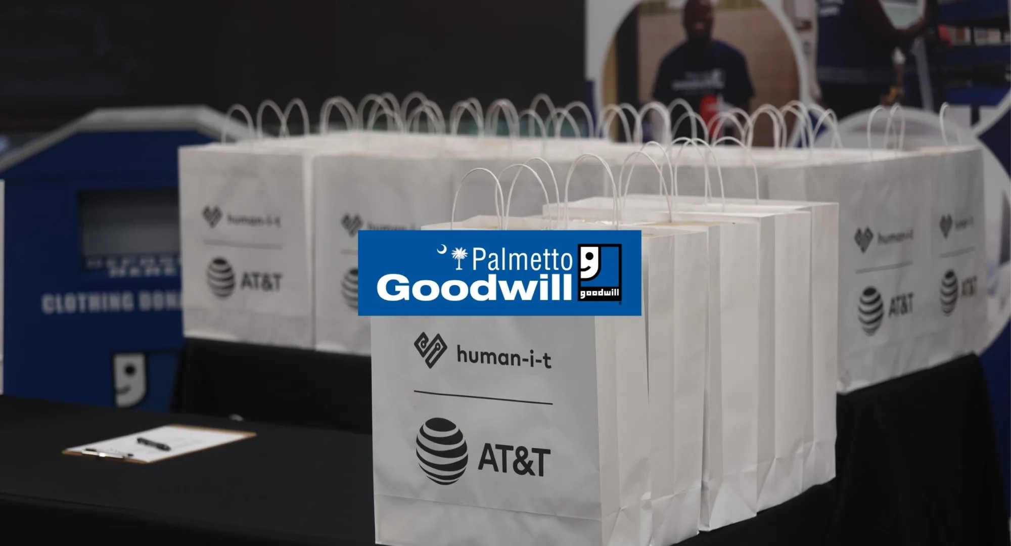 Palmetto Goodwill logo above giveaway bags from AT&T and Human-I-T, symbolizing the partnership to bridge the digital divide with laptops and digital access job training.