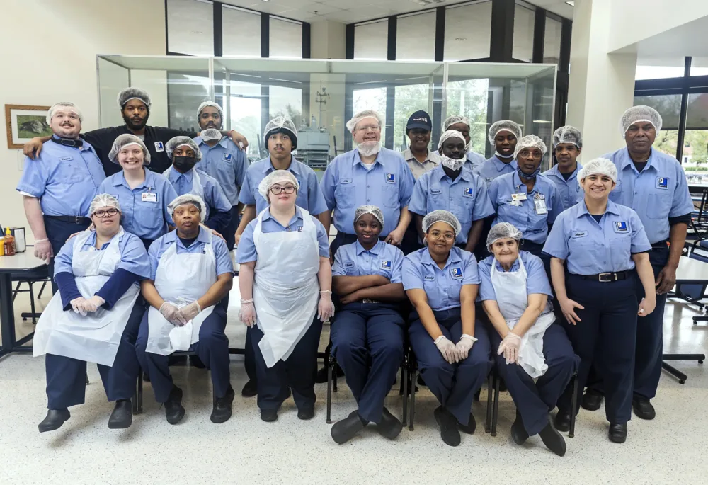 Large group photo of Palmetto Goodwill Enclave Program members and job coaches in uniform, demonstrating integrated group employment for individuals with developmental disabilities.