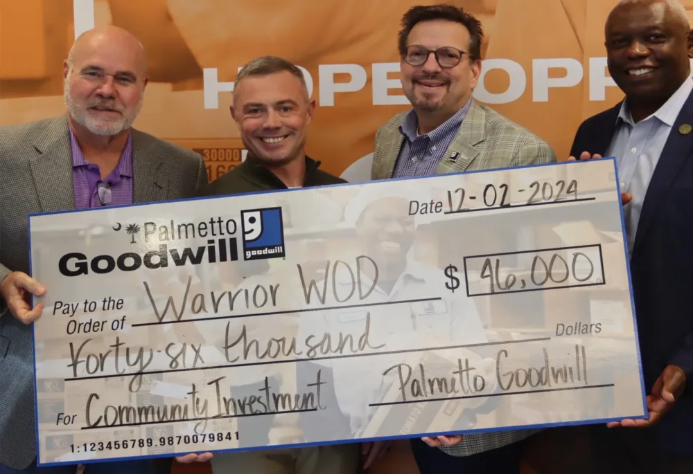Group photo of a $46,000 community investment check presentation from Palmetto Goodwill to Warrior WOD, supporting veterans with PTSD.