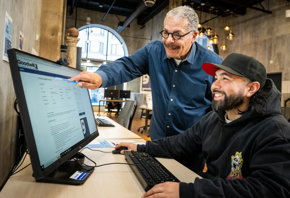 Veteran working on a computer receiving digital upskilling assistance from a mentor, leveraging PWC access to free Google Coursera certifications.
