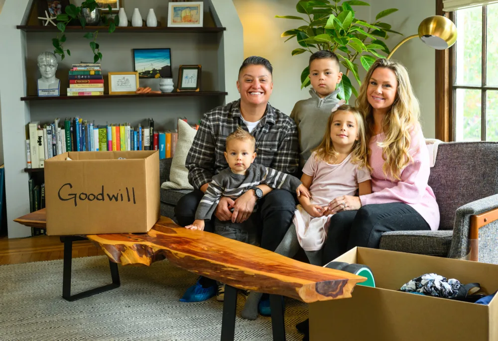 A smiling family of five in their living room packing a box labeled Goodwill with clothing and toys to donate to Palmetto Goodwill in SC.