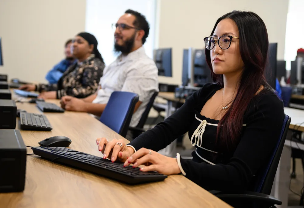 A student with glasses and dark hair working on a computer in a Palmetto Goodwill digital skills training lab in South Carolina.