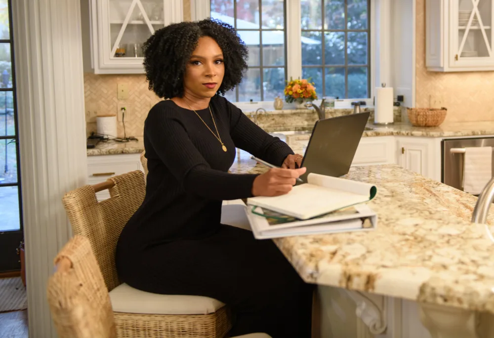A woman working on a laptop at her kitchen counter, representing how closing the digital divide in South Carolina creates measurable local impact.
