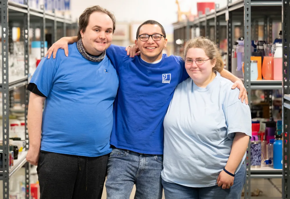 Three smiling Palmetto Goodwill team members standing together in a store aisle (demonstrating the local workforce impact of sustainable thrifting in South Carolina).