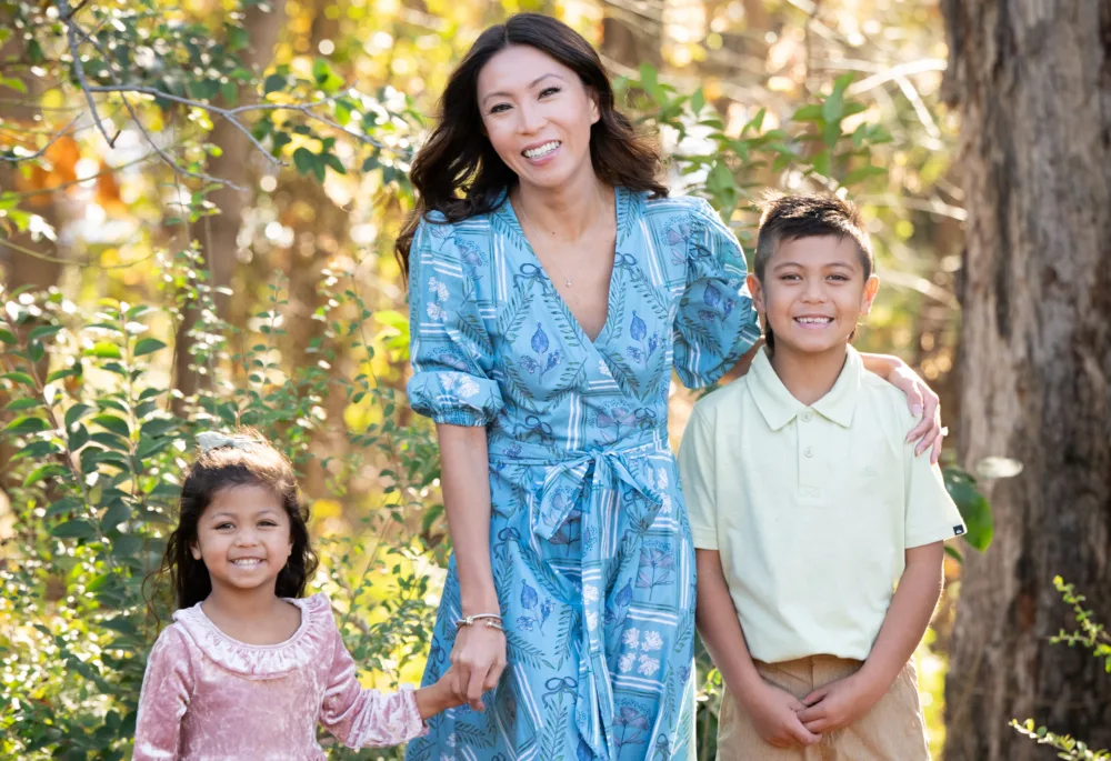 A mother and her two children smiling in a sunlit outdoor setting while wearing stylish budget kids clothes SC sourced from Palmetto Goodwill.