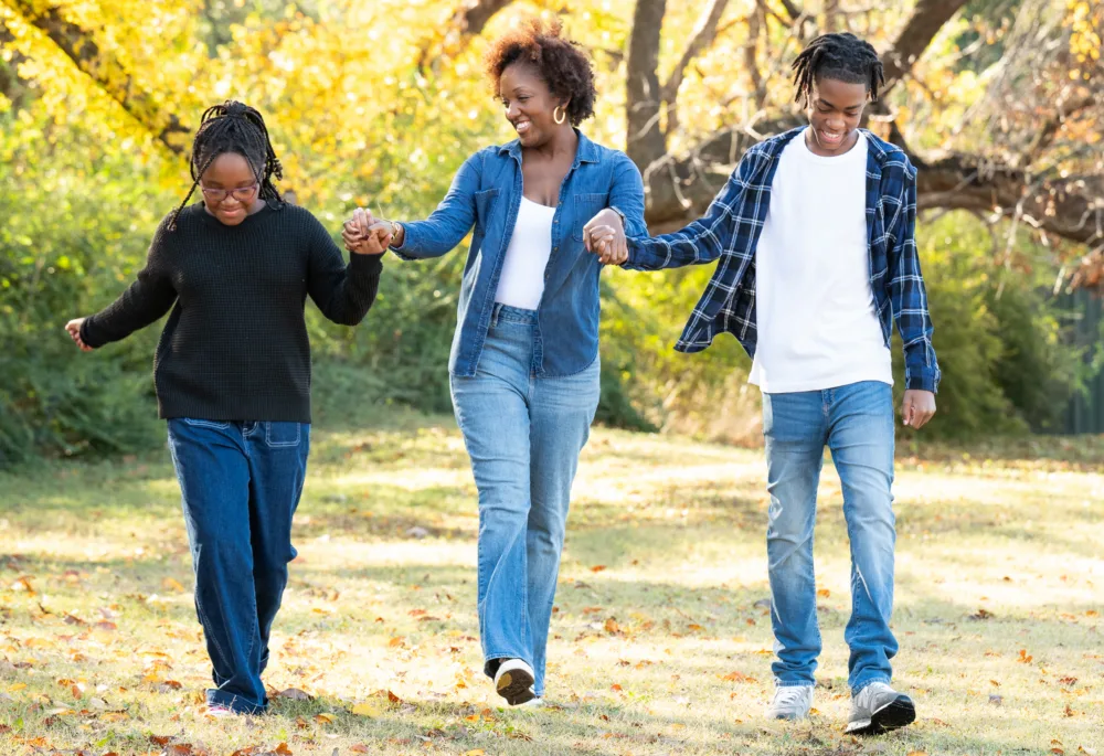 A mother walks through a park with her school-age daughter and teenage son, all wearing durable budget kids clothes SC from Palmetto Goodwill.