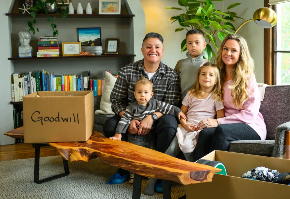 A family gathers in their living room with a "Goodwill" donation box filled with budget kids clothes SC.
