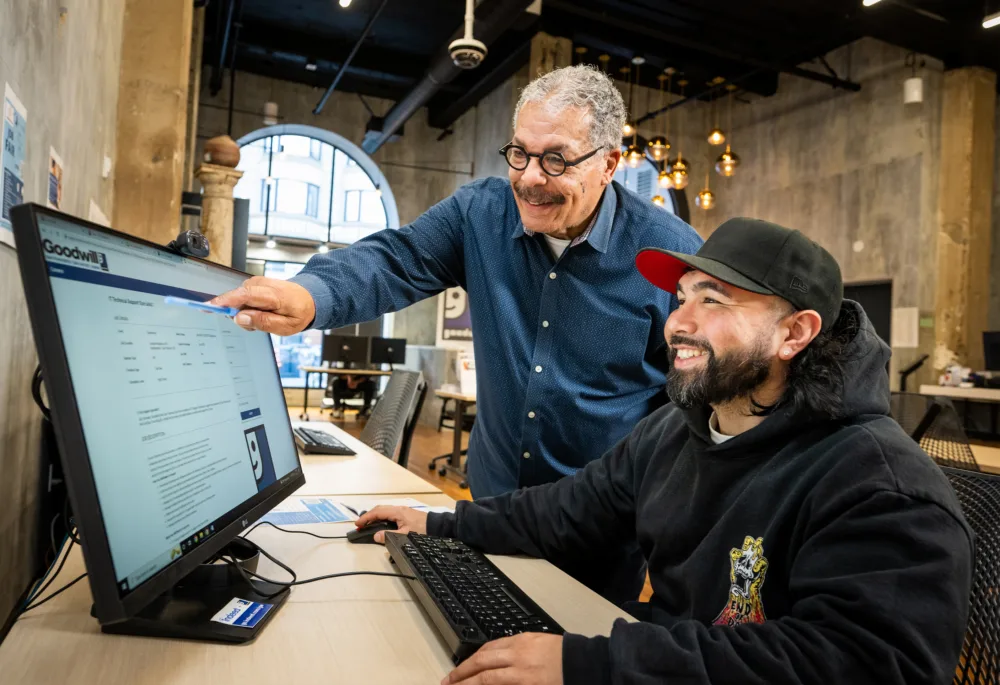 A Goodwill career mentor points at a computer screen, guiding a job seeker as they receive free resume help SC to refine their resume content.