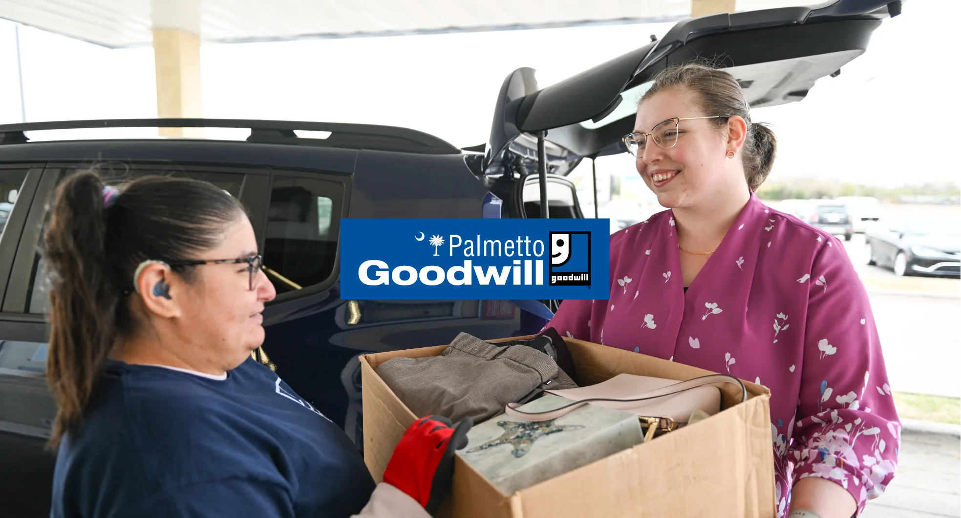 A donor handing a box of gently used clothes and household goods to a Palmetto Goodwill team member at a South Carolina donation center.