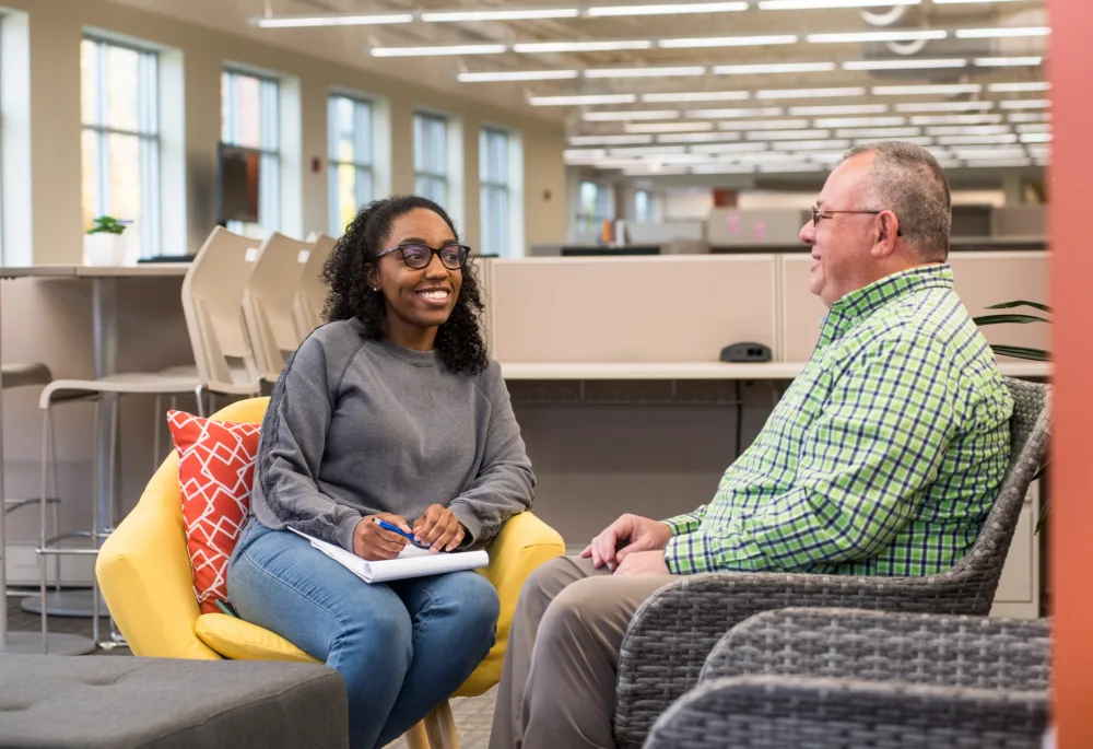 A career counselor with a notepad smiling while talking to a man in a professional office setting.